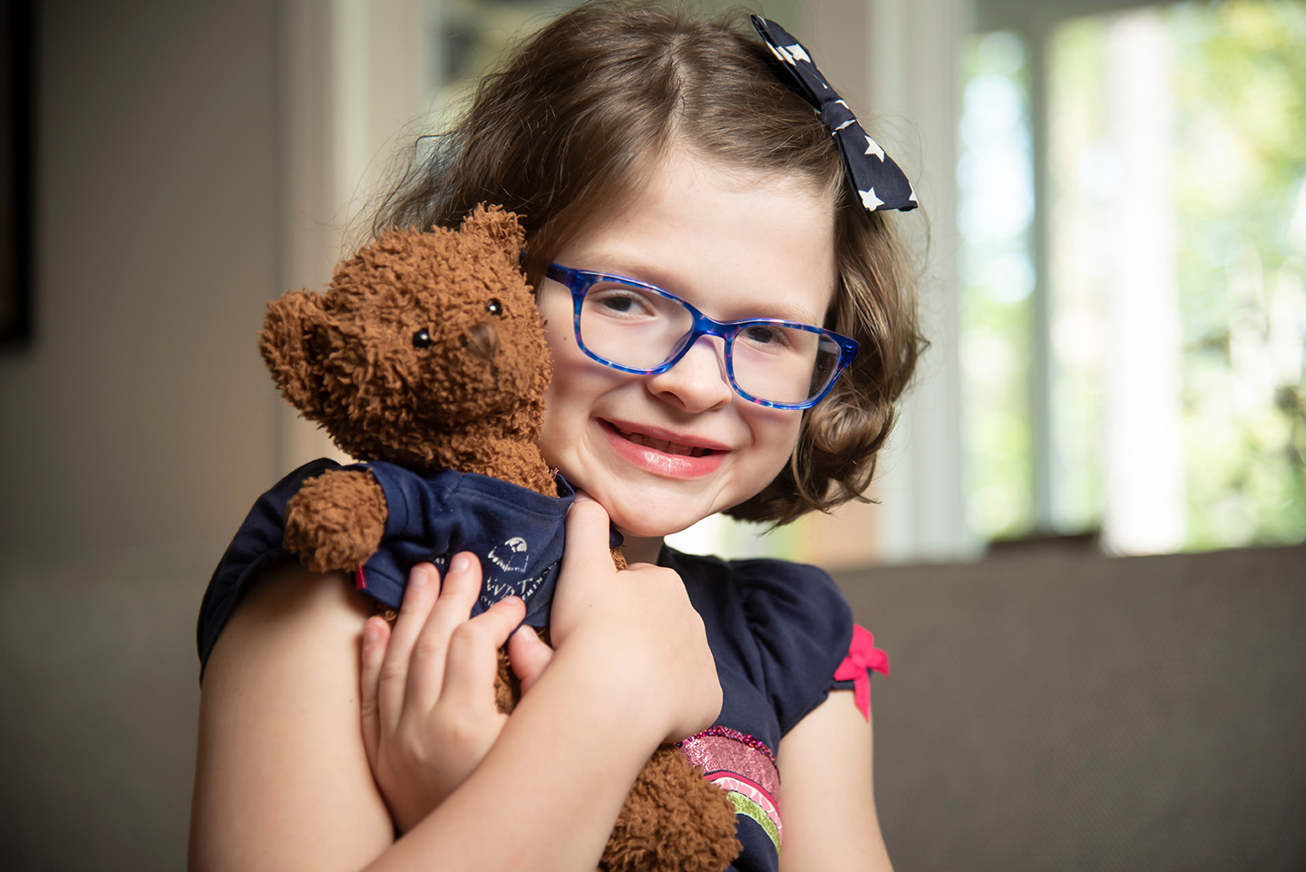 A little girl with glasses holding a stuffed bear