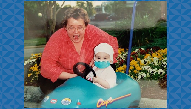 A woman kneels next to a child in a kiddie car, the child is wearing a mask