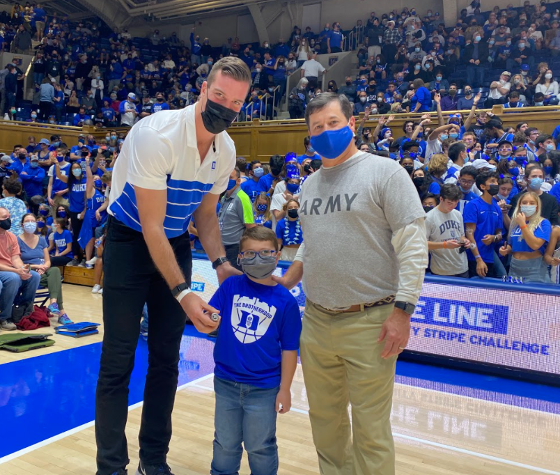 Two men standing with a young boy. All are wearing face masks and Duke Men's Basketball shirts. 