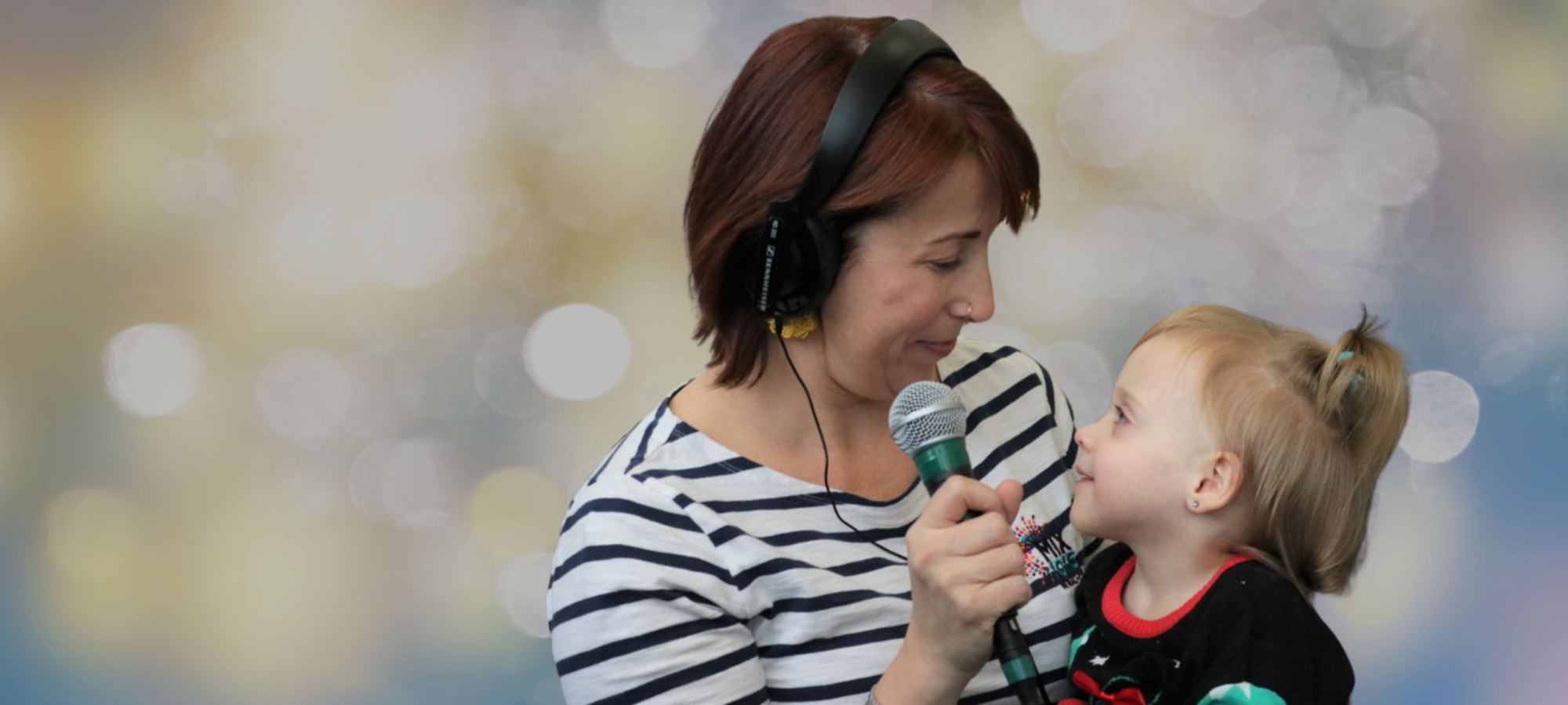 A woman wearing headphones and holding a microphone looks down at a small young child