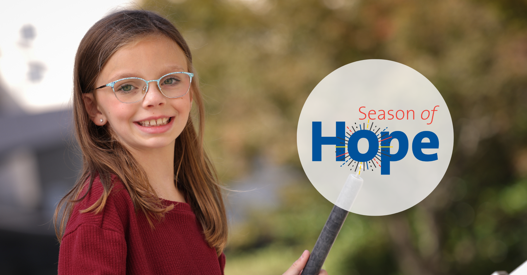 Bella, a 9-year-old little girl, smiles at the camera. She wears glasses, has a shoulder-length straight brown hair, and wears a reddish top. The image also has the words "Season of Hope" on it. 