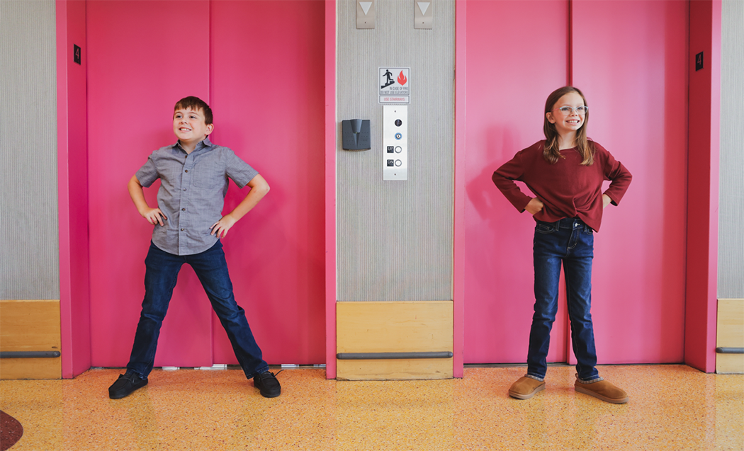 Bella and Gio stand in front of the pink elevators at Duke Children's