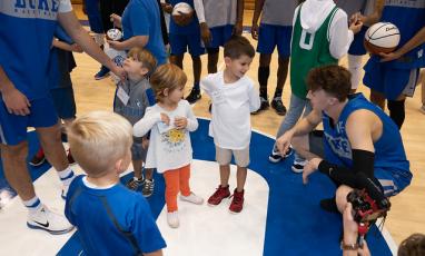 A Duke Men's Basketball player crouches and talks to a group of children. 