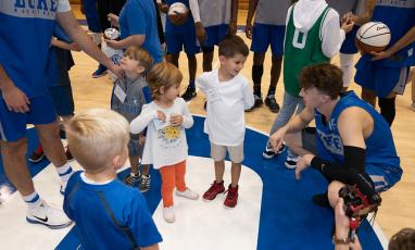 A Duke Men's Basketball player crouches and talks to a group of children.