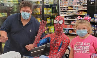 A Spider-Man and two shoppers wearing masks pose together