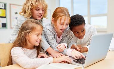 A group of kids hovers around a laptop. 
