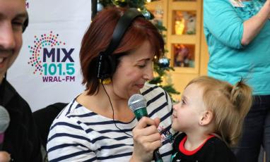 A woman wearing headphones and holding a microphone smiles down at a small child.
