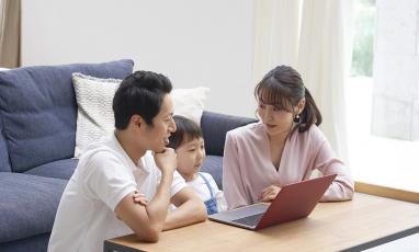 Two parents and a child sit together with a laptop, all members of the family are Asian.