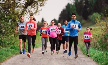 A diverse group of runners (in age, race, and gender) run down a dirt road.