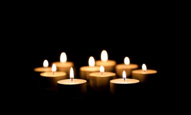 A bunch of lit votive candles in a black background. 
