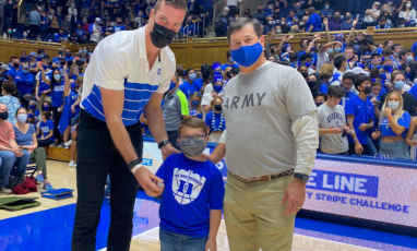 A photo of Duke basketball's Marshall Plumlee, Duke Children's patient Creed, and another representative inside Cameron Indoor Stadium. 