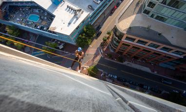 Looking down from the top of a building as a man rappels down the side of a building in Downtown Durham